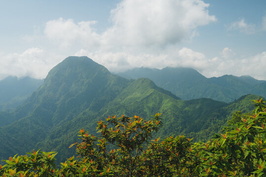 Panoramic view of lush green mountain peaks covered in vegetation under a cloudy blue sky