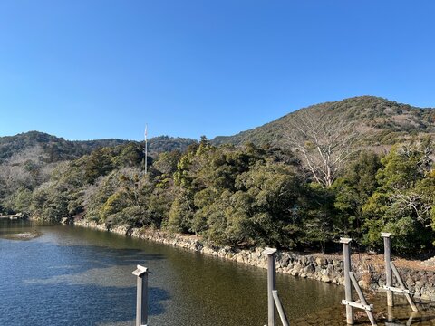 Clear Isuzu River flowing past evergreen forested hills under a blue winter sky near Ise Grand Shrine, Mie, Japan
