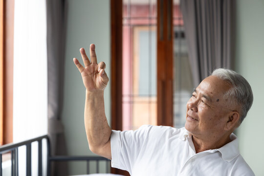 70s senior southeast asian man smiling and looking up with a happy expression, showing ok or okay hand sign at home