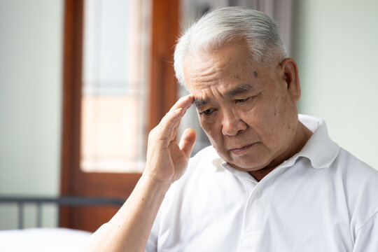 70s senior southeast asian man with white or gray hair  feeling sick with one sided headache at home, holding his temple in pain