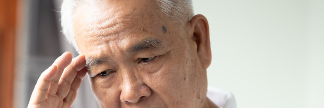 70s senior southeast asian man with white or gray hair  feeling sick with one sided headache at home, holding his temple in pain, head closeup shot