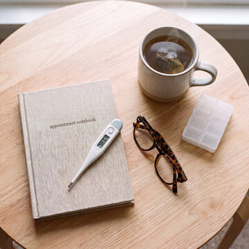 Appointment notebook and thermometer with tea on wooden table