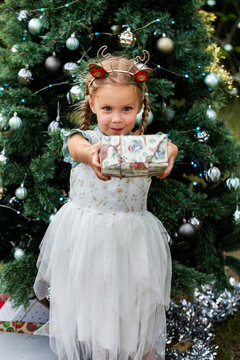 young girl holding out a wrapped gift at Christmastime outdoors by a christmas tree