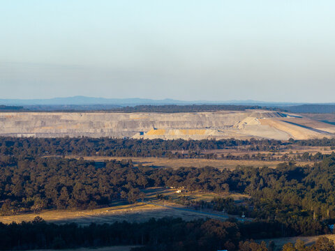 open cut coal mine on horizon in Hunter Valley seen over treetops from Bulga