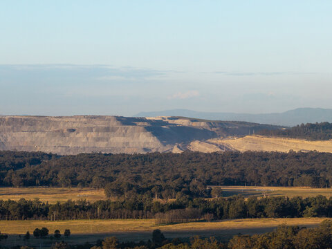 open cut coal mine on horizon in Hunter Valley seen over treetops from Bulga