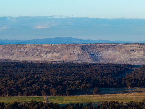 open cut coal mine on horizon in Hunter Valley seen over treetops from Bulga