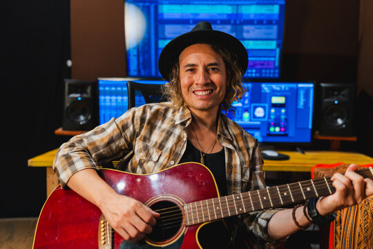 Male musician looking at camera and playing acoustic guitar in recording studio