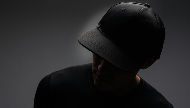 Three-quarter view blank black baseball cap snapback mockup on man with dramatic rim light against dark studio background