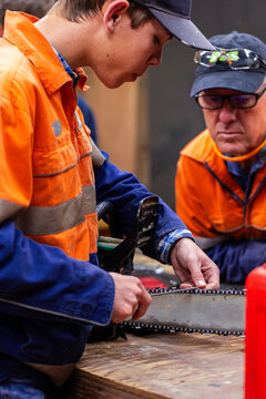 apprentice learning how to use file to sharpen chainsaw before work