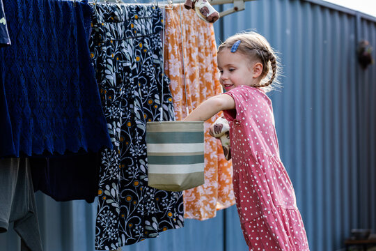 Young child on step stool helping hang out washing on outdoor line in backyard