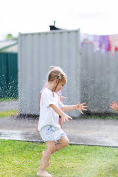 Little girl running under sprinkler spray in Australian backyard on summers day