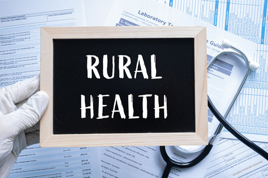 Rural Health text on black chalkboard held by gloved hand with stethoscope and medical documents, healthcare concept