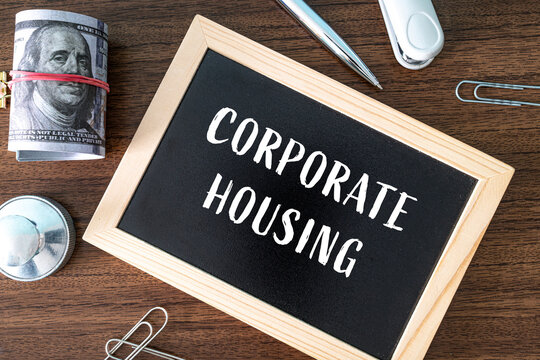Corporate Housing text on black chalkboard with dollar bills and office supplies on wooden desk, real estate concept