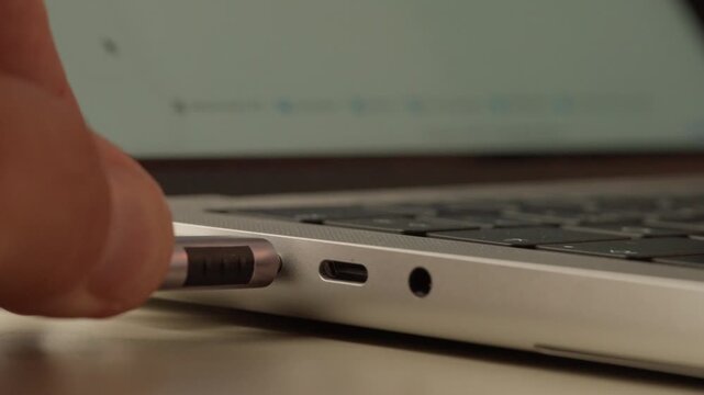 Extreme close-up of a USB-C cable being inserted into a laptop port beside the headphone jack.