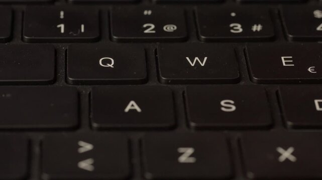 Extreme close-up of a finger pressing keys on a black laptop keyboard, showing letter and number keys in sharp detail.