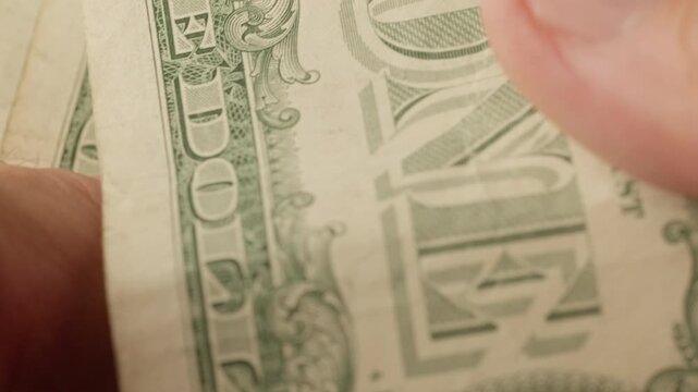 Extreme close-up of fingers touching and moving a US one dollar bill, revealing detailed printed text and texture.