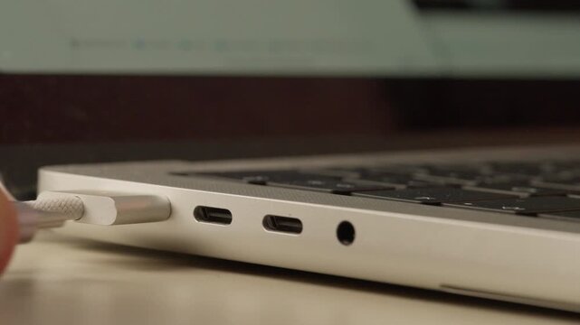 Extreme close-up of a white cable being unplugged from the USB-C port on the side of a laptop.