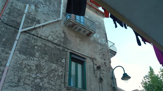 A worn stucco apartment wall with balconies and laundry lines frames a quiet residential corner in southern Italy.