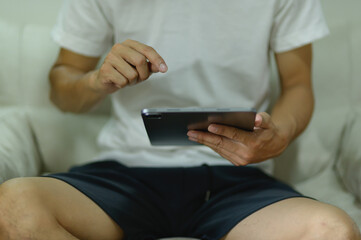 Man Using a Digital Tablet While Sitting on Couch in Casual Clothing © AK ST
