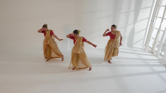 Three Indian women performing a traditional dance in a bright, spacious room