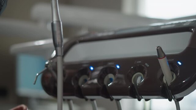 Close up of man hand reaching for and grasping orthodontic scaler tool from its holder in soft lighting. arm is partially visible wearing dark fabric with green sleeve while dental equipment