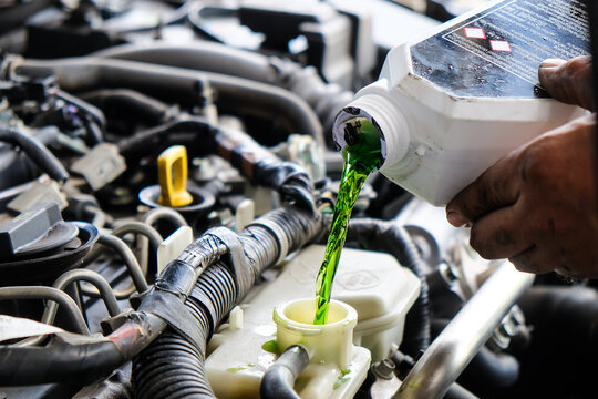 Mechanic adding green antifreeze liquid to a car engine during maintenance