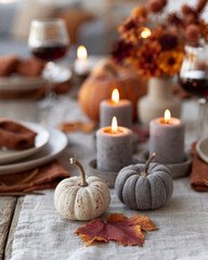 Obraz premium Cozy autumn table bathed in candlelight. Candles flicker beside rustic pumpkins and leaves. Wine glasses hold deep red wine, softly blurred. Plates rest on linen, surrounded by warm tones