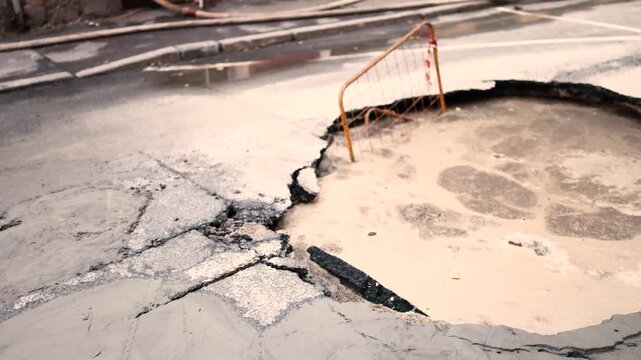 Large sinkhole collapses street surface with warning barrier nearby