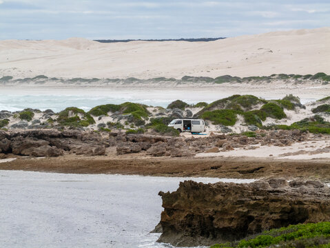 Camper van near remote beach with sand dunes and surf