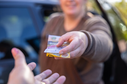 Person handing over cash bank notes to another hand during financial transaction outdoors