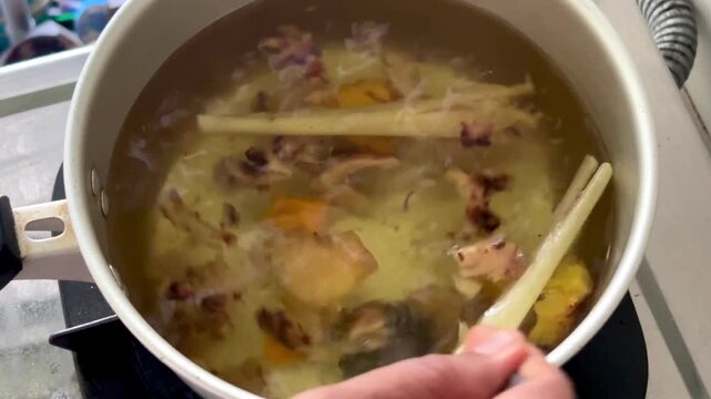 An Asian man is stirring a traditional herbal decoction&mdash;a drink made from a blend of spices: red ginger, galangal, turmeric, and lemongrass.