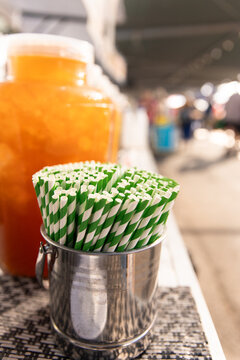 Metal container filled with green‑and‑white striped paper straws sits on a market counter