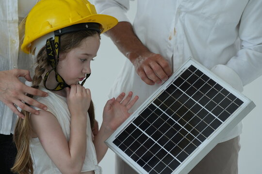 Young parents teaching their curious child let the girl in a toy helmet touch the photovoltaic cells up close in the bright interior of their newly built home in warm natural light
