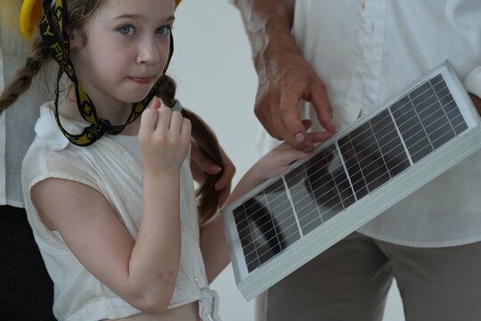 Caucasian family of three with a small photovoltaic module let the girl in a toy helmet touch the photovoltaic cells up close inside their new energy efficient home