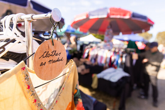 Close‑up of a handwritten wooden sign that reads &ldquo;clothes as marked" on a clothing rack