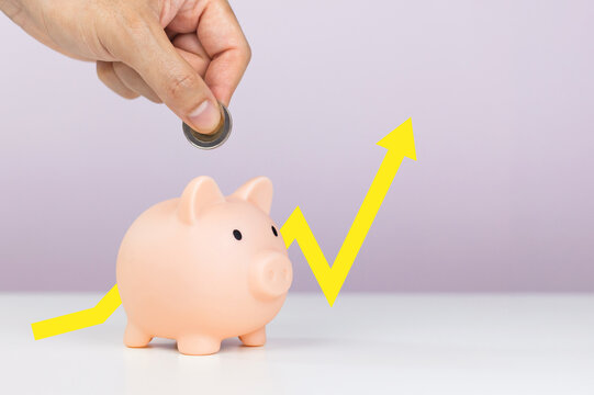 Hand saving a coin into a pink piggy bank beside a yellow rising arrow graph line, representing compound interest, investment return and capital growth