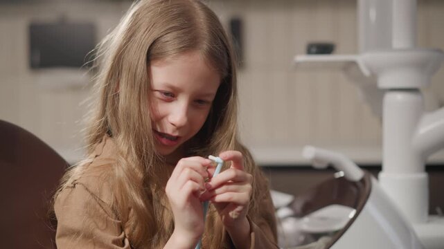 Close up of young girl holding dental floss in orthodontic clinic setting. Girl appears to be preparing for or following teeth cleaning procedure with professional equipment visible