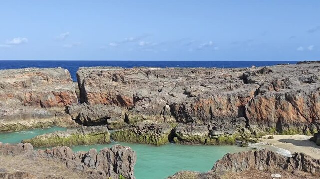 Natural turquoise tidal pool surrounded by rugged coastal rocks with deep blue ocean and clear tropical sky in the background