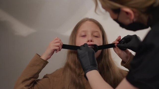 Young girl receives dental examination with braces. professional wearing black gloves adjusts oral retractor to reveal child teeth focusing on orthodontic treatment in clinical setting