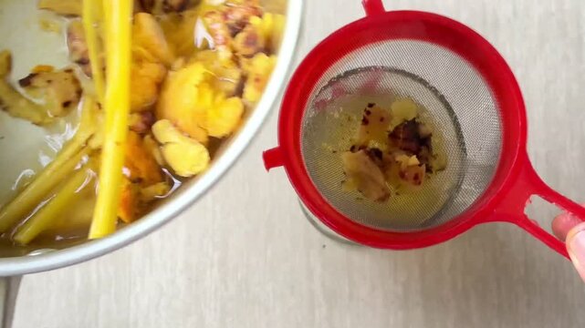 The process of straining a traditional herbal concoction&mdash;a drink made from a blend of spices such as red ginger, galangal, turmeric, and lemongrass&mdash;as it is poured into a glass.