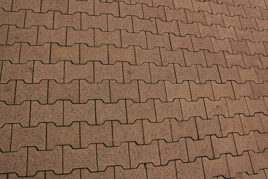 Reddish interlocking concrete pavers forming a repeating geometric pavement pattern with dark joints and subtle surface wear.