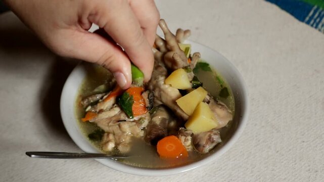 A hand squeezing fresh lime juice into a bowl of chicken feet soup, adding a sour citrus flavor to the warm dish.