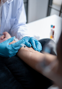 Female phlebotomist collecting blood sample from patient with needle for laboratory testing at medical clinic.