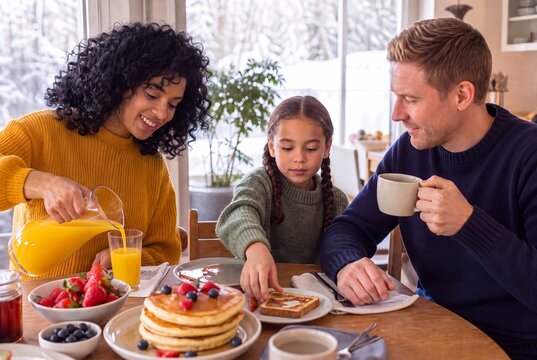 Adults and child sharing pancakes and juice at breakfast