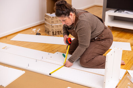 Adult woman kneeling on a polished wooden floor measuring a white furniture panel
