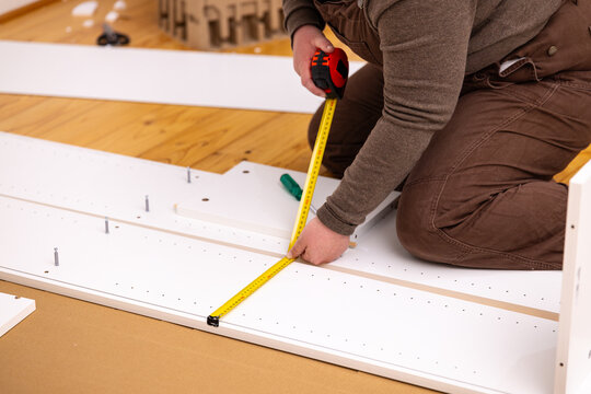 Adult woman kneeling on a polished wooden floor measuring a white furniture panel