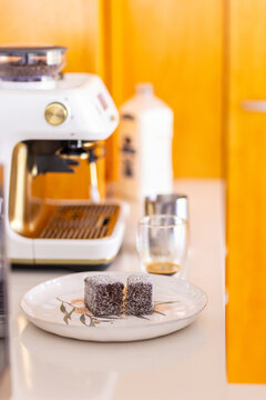 Lamingtons served on plate beside espresso shot and coffee machine in kitchen