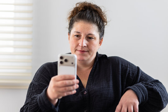 Woman in black shirt holding smart phone looking attentively at screen indoors