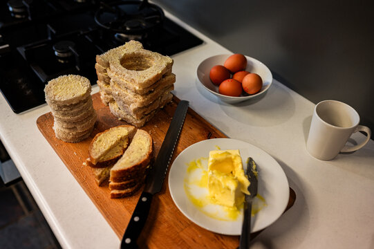 Bread and butter sit on a wooden board with eggs nearby in a kitchen preparing for breakfast
