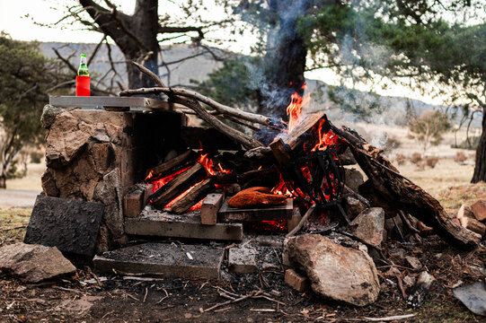 A piece of meat is placed on a woodfire barbecue surrounded by burning wood in Crackenback